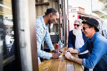 Profissional atendendo pedidos em food truck, enquanto dois cliente sorriem, simbolizando a importância e impacto dos brindes para o dia do cliente