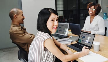 Três colaboradores usando notebook sorrindo. Dois desses colaboradores estão se entreolhando, simbolizando comunicação empresarial