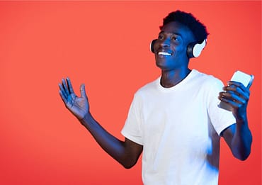 Jovem sorrindo com fone de ouvido, segurando celular, simbolizando ideias de brindes para jovens.