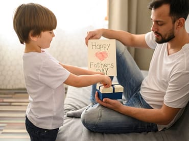 Filho pequeno entregando presente para o pai, com cartão de feliz dia dos pais. A imagem represente brinde dia dos pais para empresa