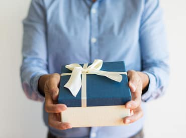 Pessoa entrando um presente (caixa creme, tampa da caixa azul com um laço creme) representando brindes úteis e criativos