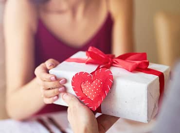 Pessoa entregando uma caixa de presente com enfeite de coração para a namorada, simbolizando um brinde para dia dos namorados