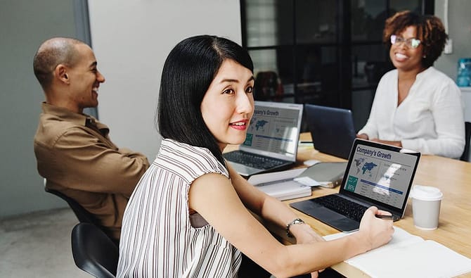 Três colaboradores usando notebook sorrindo. Dois desses colaboradores estão se entreolhando, simbolizando comunicação empresarial