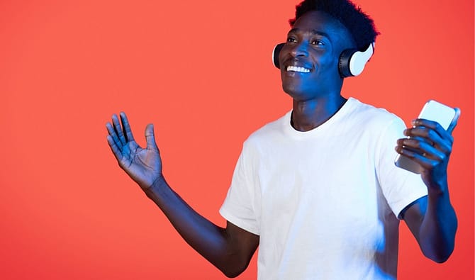 Jovem sorrindo com fone de ouvido, segurando celular, simbolizando ideias de brindes para jovens.