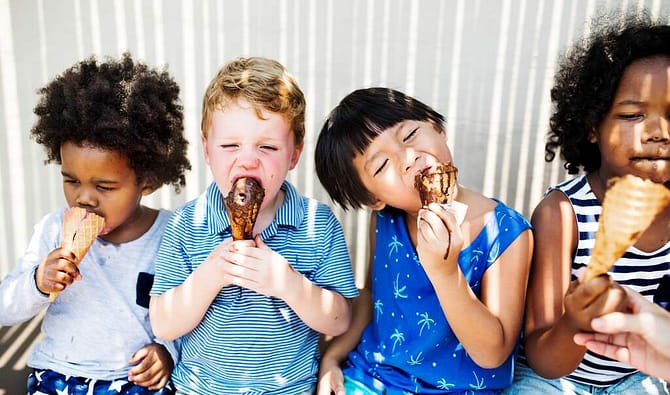 quatro crianças sentadas comendo sorvete na casquinha representando ideias de brindes para o dia das crianças
