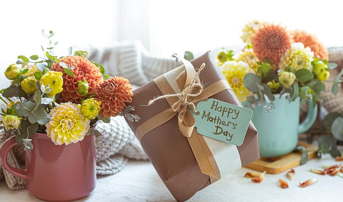 Simbolizando brinde dia das mães corporativo: Embrulho de caixa de presente com etiqueta escrito "Happy Mothers Day" (Feliz dia das mães, em inglês), com vasos de flores ao redor