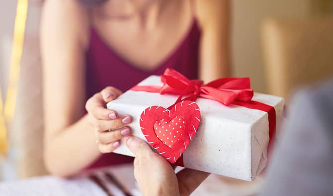 Pessoa entregando uma caixa de presente com enfeite de coração para a namorada, simbolizando um brinde para dia dos namorados