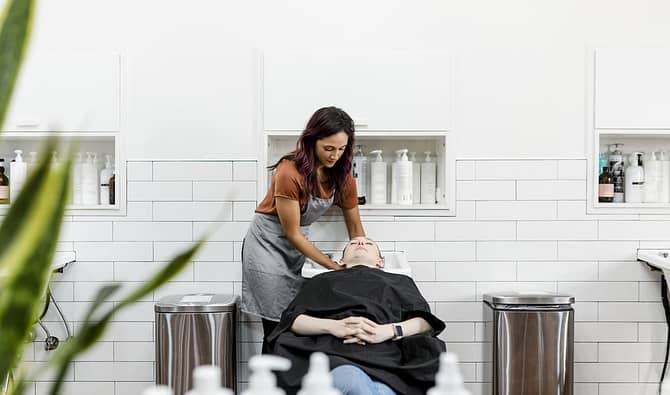 Cabeleireira em salão de beleza lavando cabelo da cliente, simbolizando a importância de fidelizar clientes através de lembrancinhas e mimos