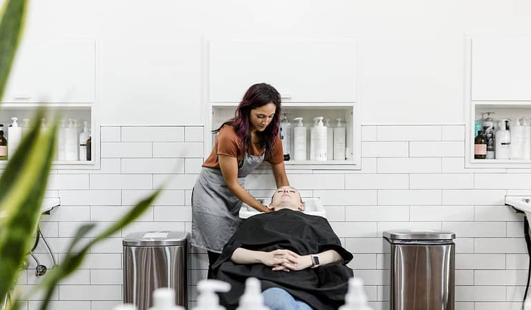 Cabeleireira em salão de beleza lavando cabelo da cliente, simbolizando a importância de fidelizar clientes através de lembrancinhas e mimos