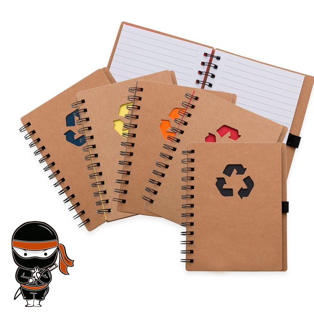 Cadernos ecológicos, com símbolo colorido de reciclagem na capa, mascote da Ninja Brindes desenhado no canto inferior esquerdo da imagem, em posição de agradecimento ou cumprimento, com as mãos juntas