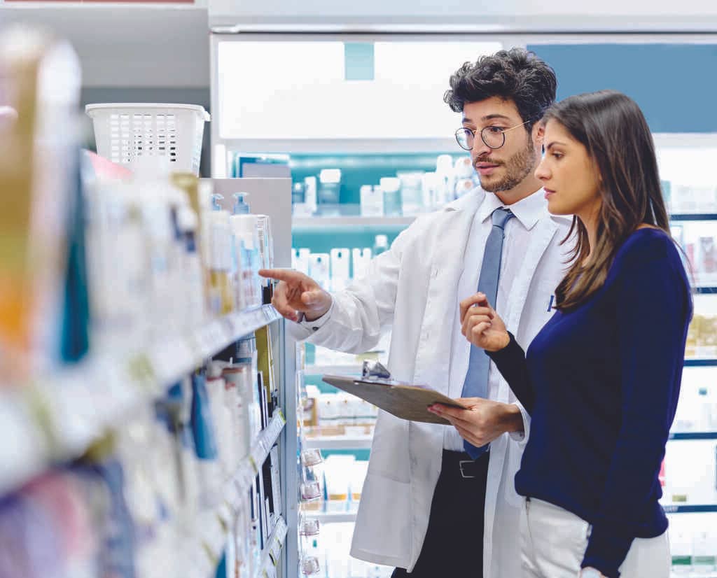 Farmacêutico com óculos de grau, segurando prancheta, mostrando produtos numa prateleira para uma cliente atenta, simbolizando como escolher ações promocionais de sucesso