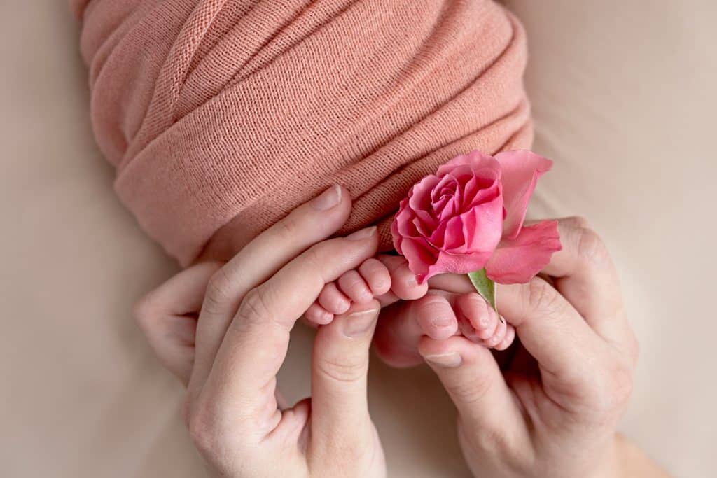 Mãos segurando pés de bebê com flor, simbolizando dia dos pais e dia da mães, que são datas importantes para dar brindes