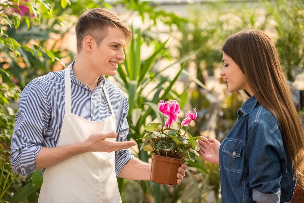 Homem de avental dando um vaso com flores para cliente, simbolizando ideias criativas de mimos para cliente fiel
