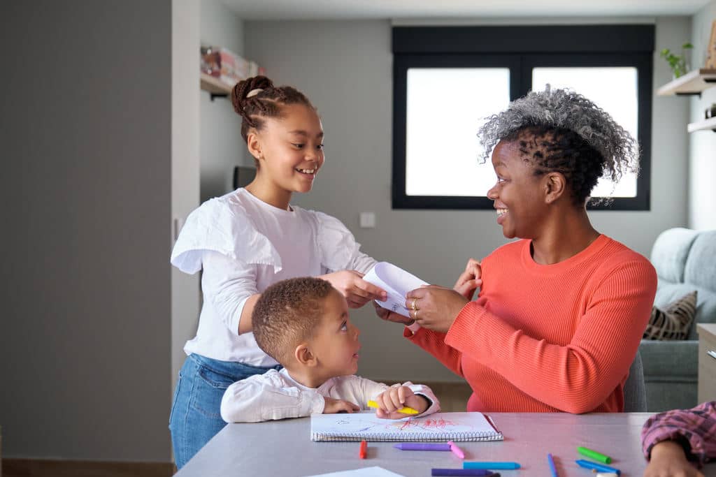 Filho pequeno e filha criança presentando a mãe sorridente com desenhos coloridos que eles fizeram