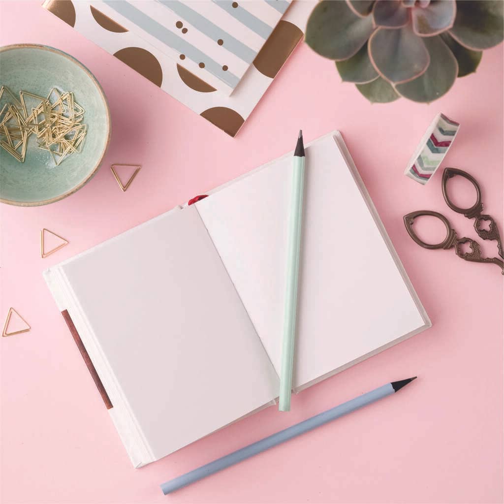 mesa com caderno e acessórios de escritório representando ideias de brindes para outubro rosa